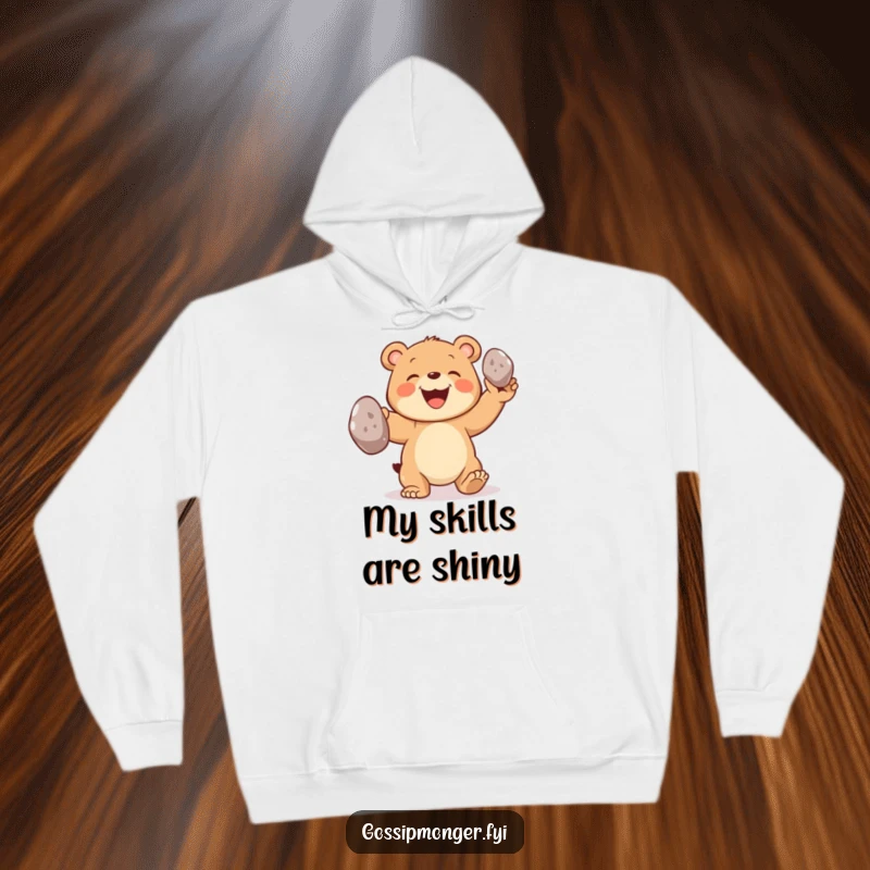 Funny bear hoodie featuring a joyful bear cub with a big grin, skillfully juggling three oversized shiny pebbles.